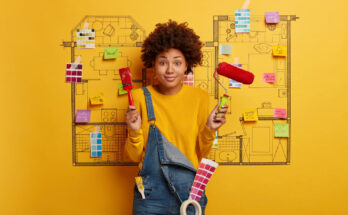 Mlada ženska z orodjem v rokah stoji pred rumeni steno